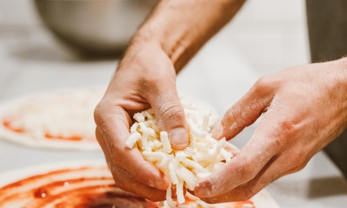 Hands placing cheese on homemade pizza dough